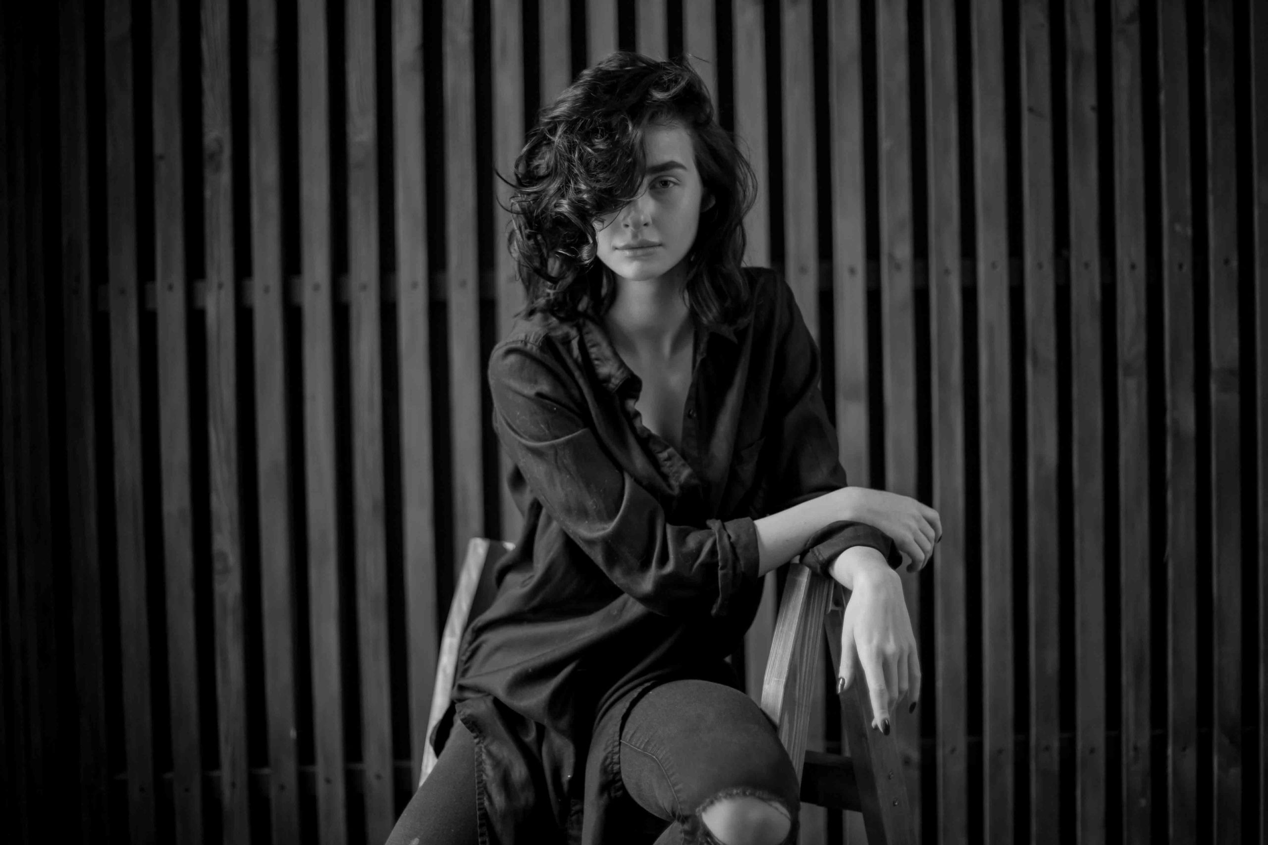girl-with-curly-dark-hair-natural-makeup-sitting-dark-leather-chair-black-white-photo